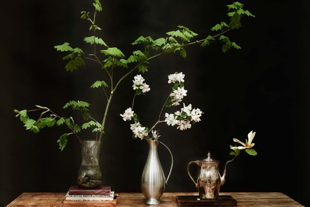 Still LIfe on dark background. Vase full of stones, Maple branch, Sketchbooks, Silver Urn with Flowers